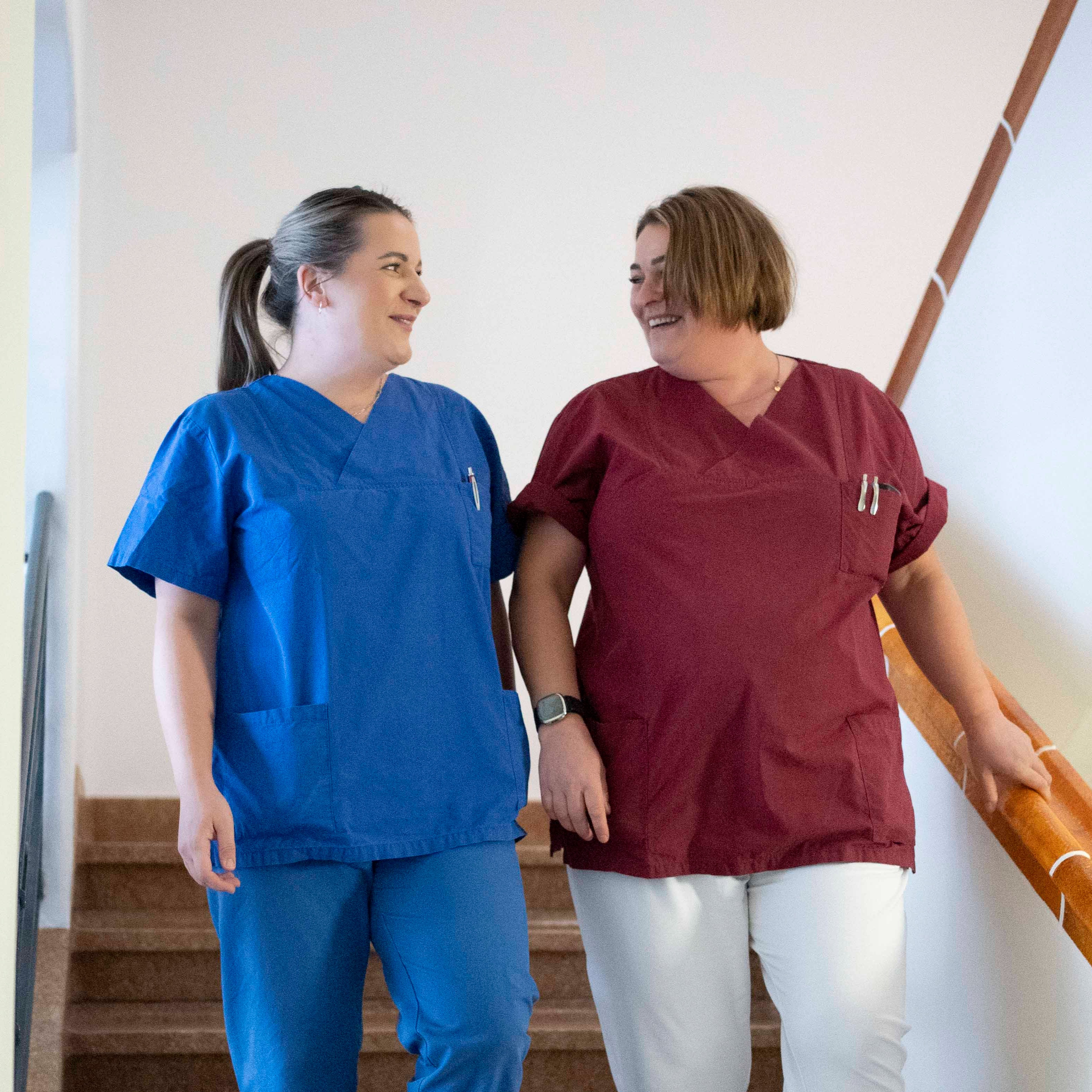 Zwei medizinische Fachkräfte stehen in einem Krankenhausflur, sprechen miteinander und wirken freundlich und konzentriert.