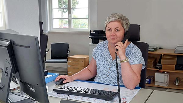 Eine Mitarbeiterin der Patientenaufnahme sitz am Schreibtisch und telefoniert.