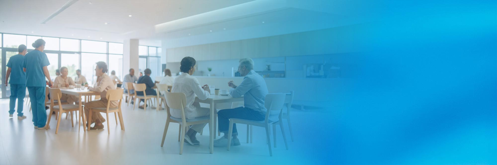 Eine lebendige Szene in der Cafeteria. Das Bild verläuft von links nach rechts zu einem Blauverlauf.