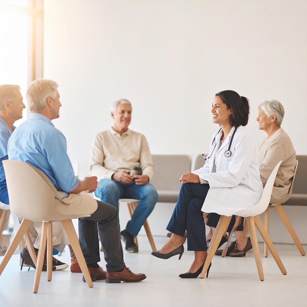 Ärztin im weißen Kittel leitet eine Gruppentherapie mit vier älteren Patienten im Stuhlkreis