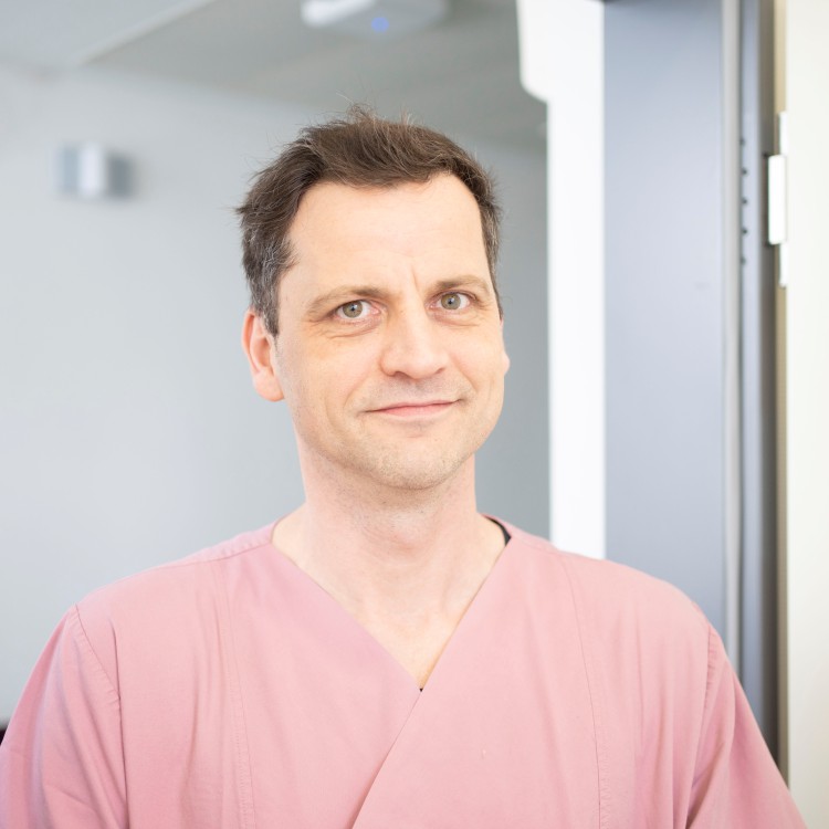 Ein freundlicher Pfleger in roter Dienstkleidung lächelt in die Kamera