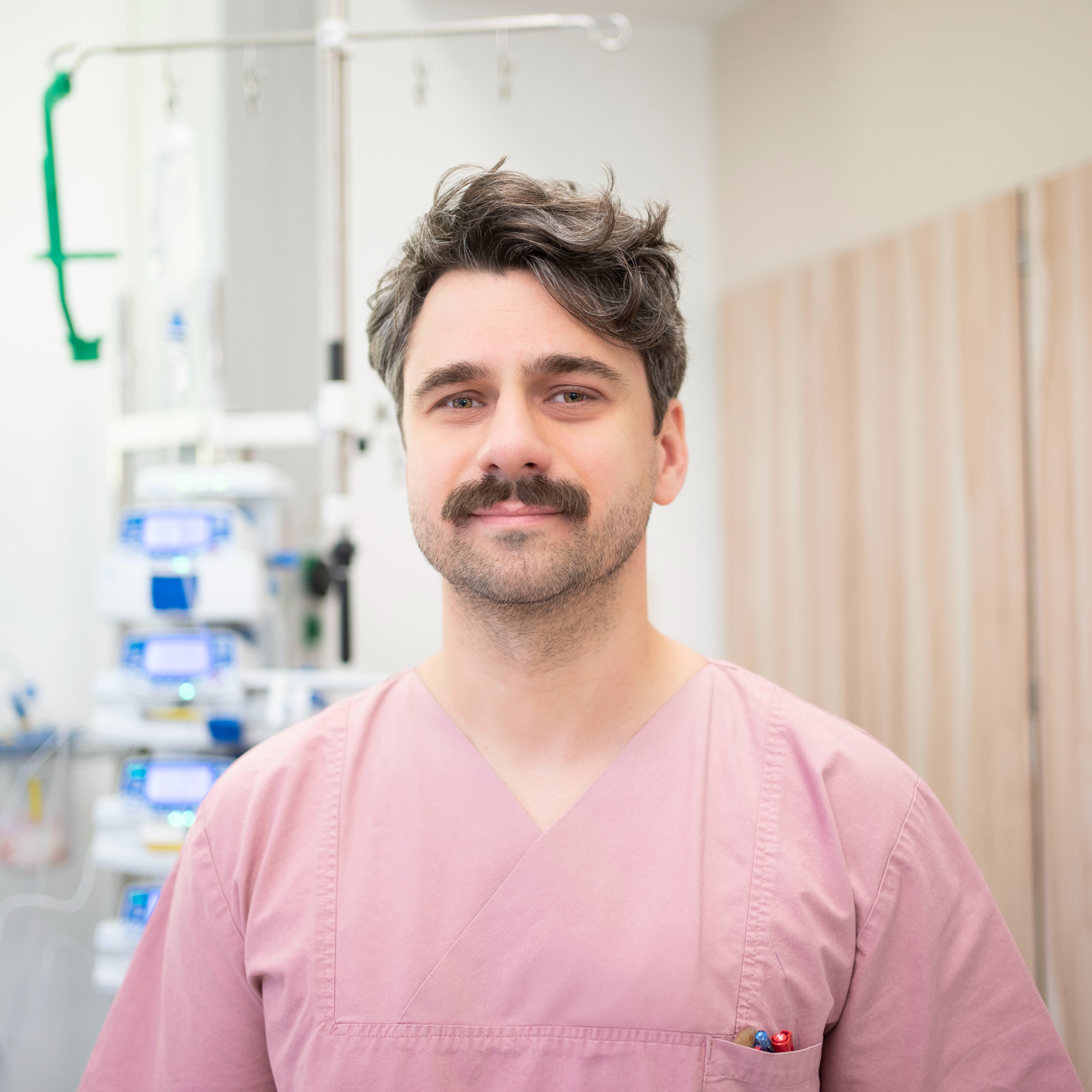 Ein freundlicher Pfleger in roter Dienstkleidung lächelt in die Kamera